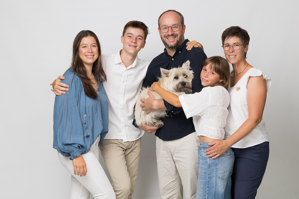 Familia con papas y sus hijos de pie con su highland white terrier, haciendo fotos de estudio